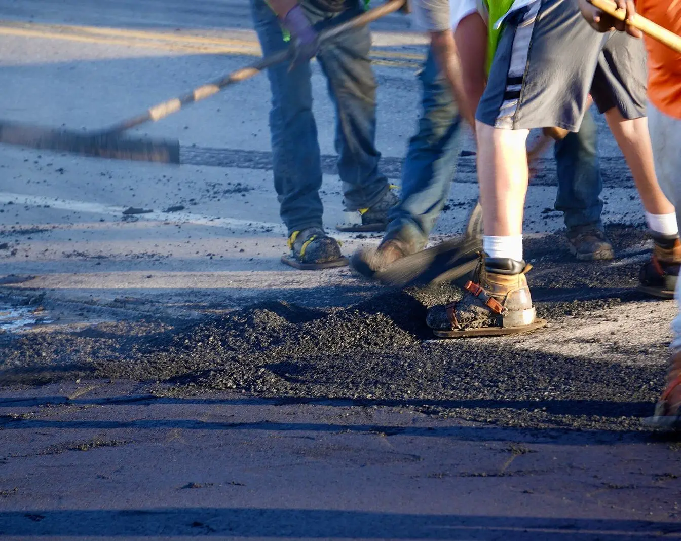 Road workers spreading and raking fresh black asphalt across a carriageway. A representative file photograph of road resurfacing work, not a picture of the repaired Ras Ghareb–Zafarana stretch.