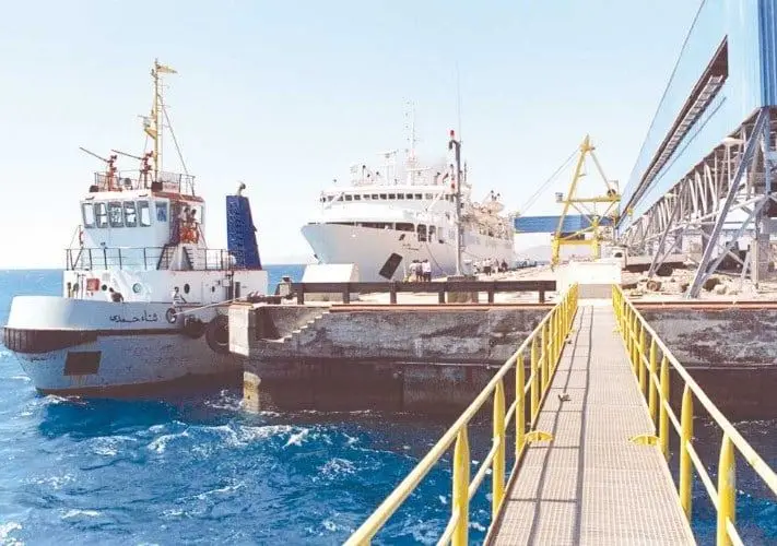 File photo of a Red Sea port quay: a small workboat and a larger white vessel moored alongside a concrete berth with a yellow-railed gangway. Published by Al Mal as a picture of Safaga port; it does not show the planned Safaga–Duba service.