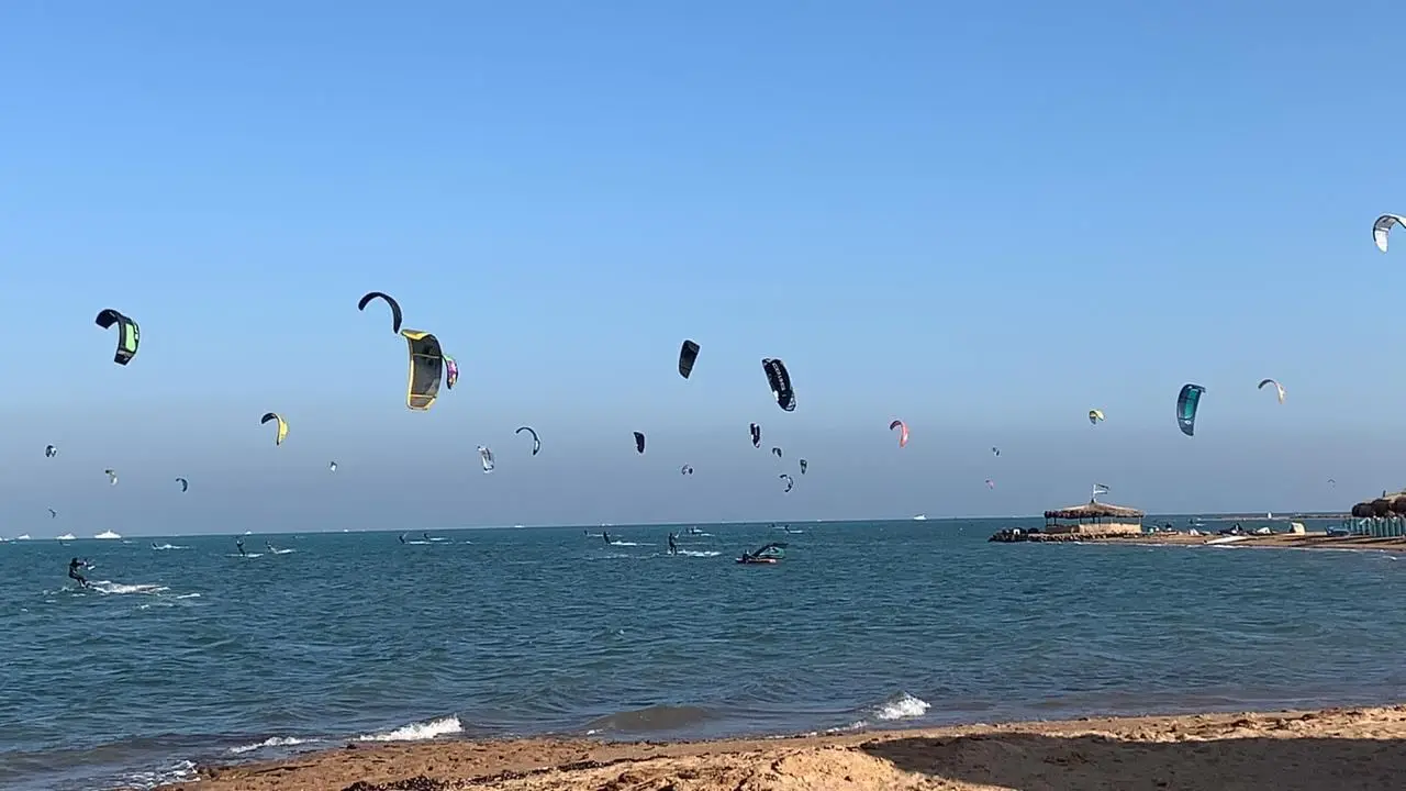Dozens of kitesurf kites in the air over a shallow Red Sea bay, with riders on the water and a sandy beach in the foreground. Photograph published by Youm7 with its report on the autumn kitesurf season.