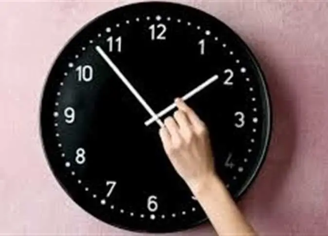 Representative file photo: a hand reaches up to move the hour hand of a large black wall clock hanging on a pink wall.