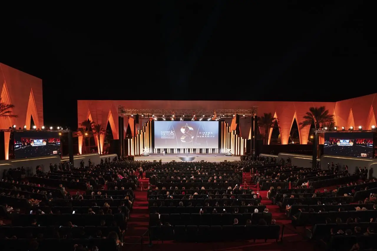 The El Gouna Film Festival's open-air auditorium at night, with a seated audience facing a lit stage and a screen carrying the festival's Cinema for Humanity branding. Published by Egyptian Streets with its report on the ninth edition; not identified as a photograph of a specific screening.