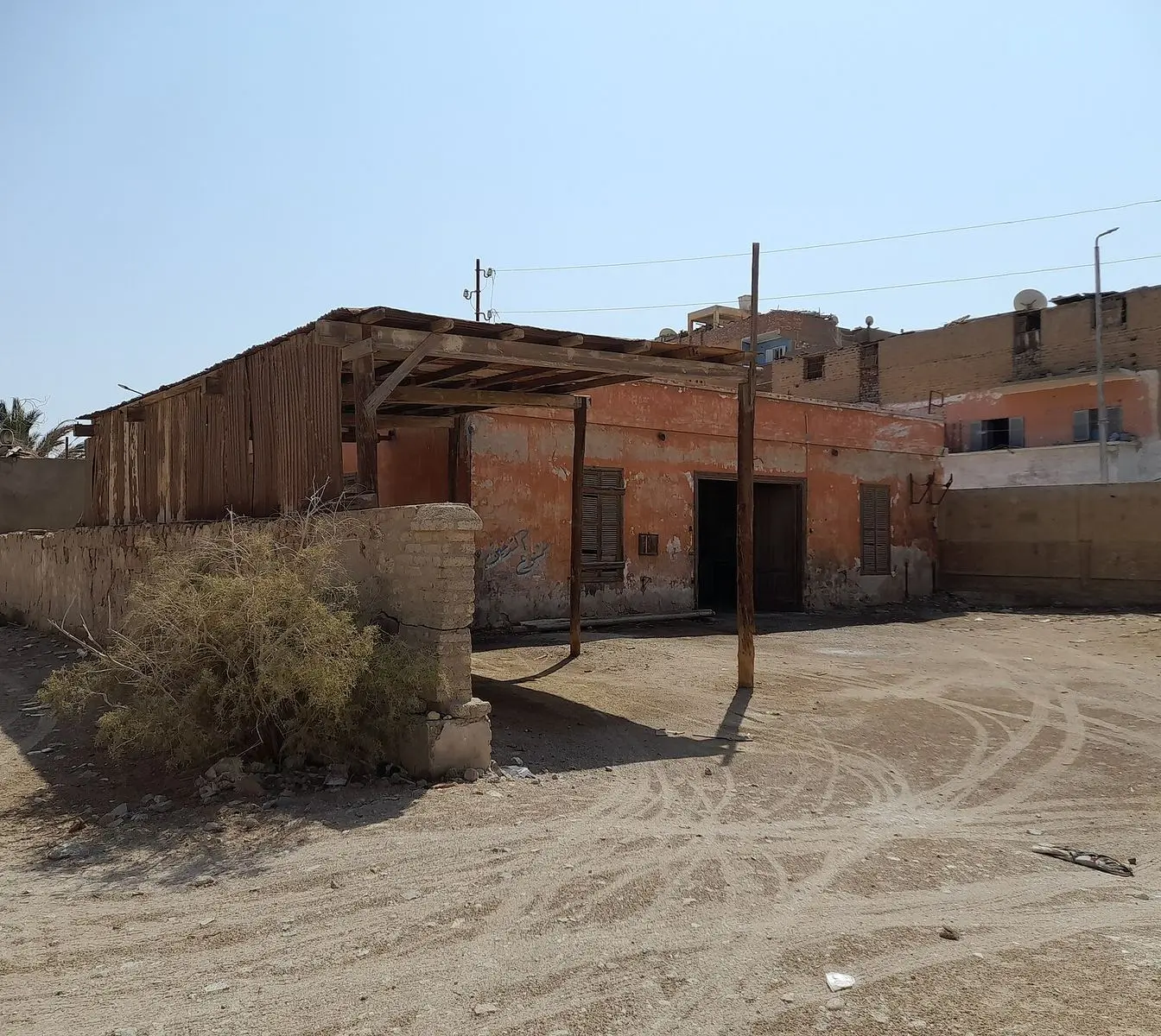Present-day photo of a derelict single-storey building with a timber canopy and a low wall on sandy ground in El Quseir, recorded on Wikimedia Commons as part of the Italian Phosphate Company site. A file photograph, not an image of the 1916 shipment.