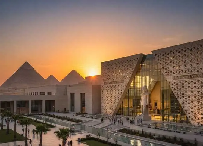The Grand Egyptian Museum at sunset, its triangular stone facade and glazed entrance hall with a tall statue inside, the Giza pyramids visible behind (file photo).