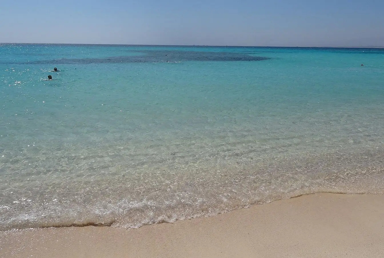 File photo of the shoreline at Giftun Island off Hurghada: clear shallow water over pale sand, a dark reef patch offshore and a few swimmers. Representative view of the coast the agreement covers, not a photograph of the signing.