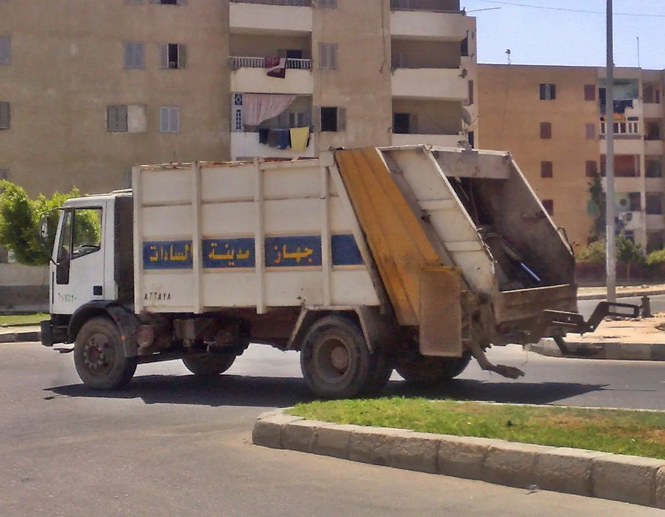 File photo of a municipal refuse lorry with its rear loader raised, driving past residential blocks in Sadat City, Egypt. A representative picture of municipal waste collection, not a photograph of the Safaga campaign.