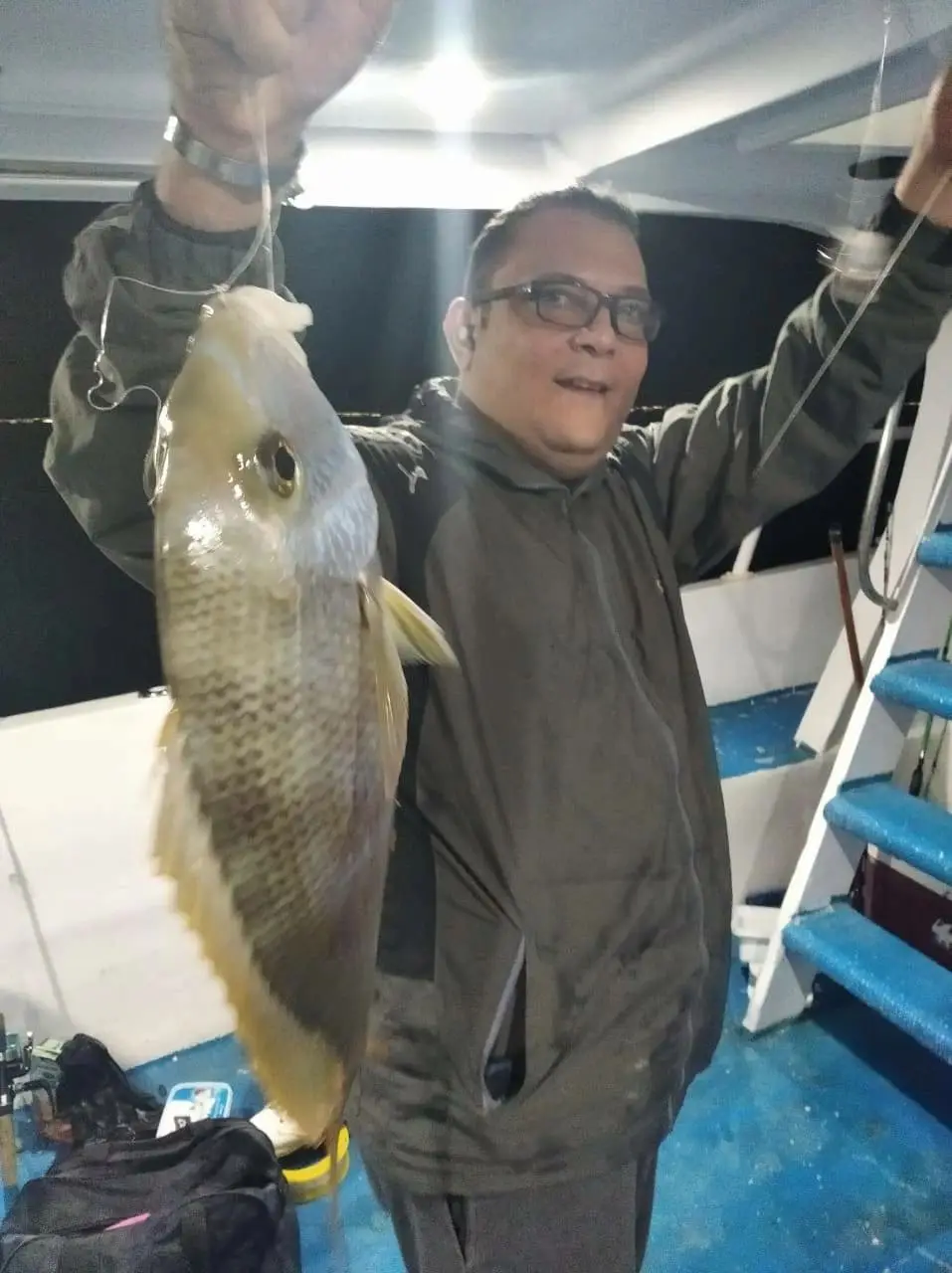 An angler in a dark jacket stands on a boat deck at night, holding up a freshly caught fish on a line. The paper ran this photograph with its report on recreational fishing trips on the Red Sea.
