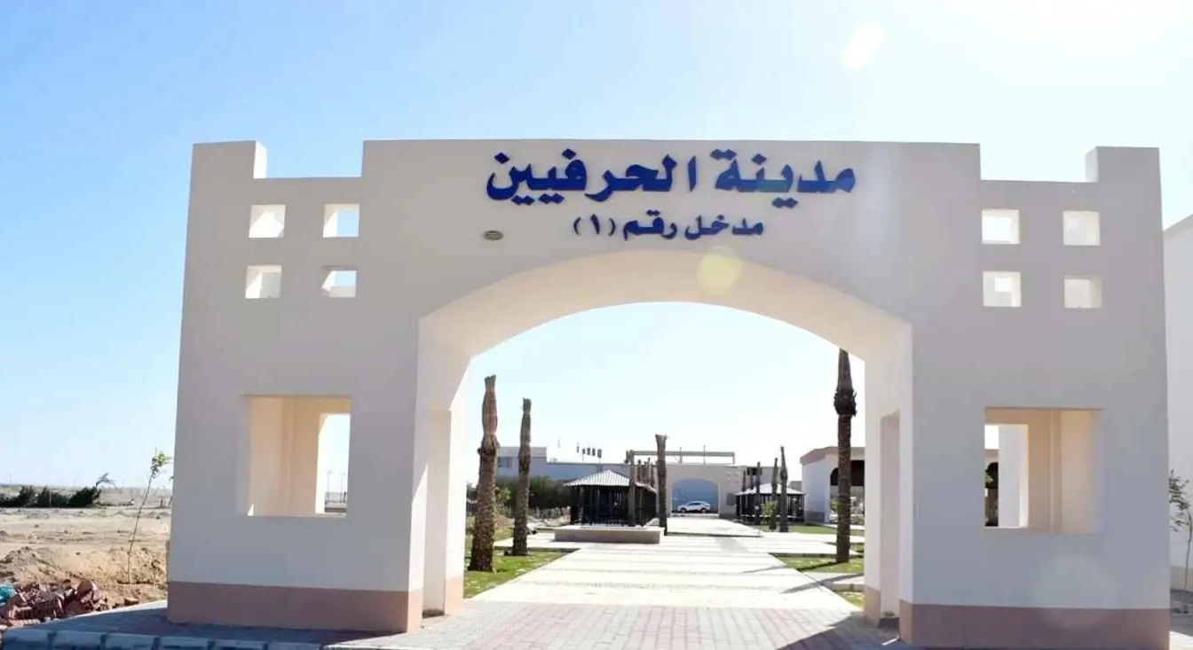 The gateway to Craftsmen City in Hurghada: a pale archway signed in Arabic "Craftsmen City, Entrance No. 1" over a paved walkway lined with palms, with low buildings behind.
