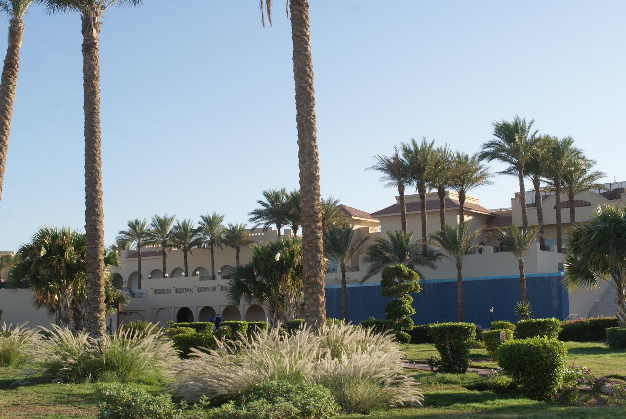 Angelegte Resortgärten mit Palmen und geschnittenen Hecken vor einem Arkadenhotel in der Makadi-Bucht