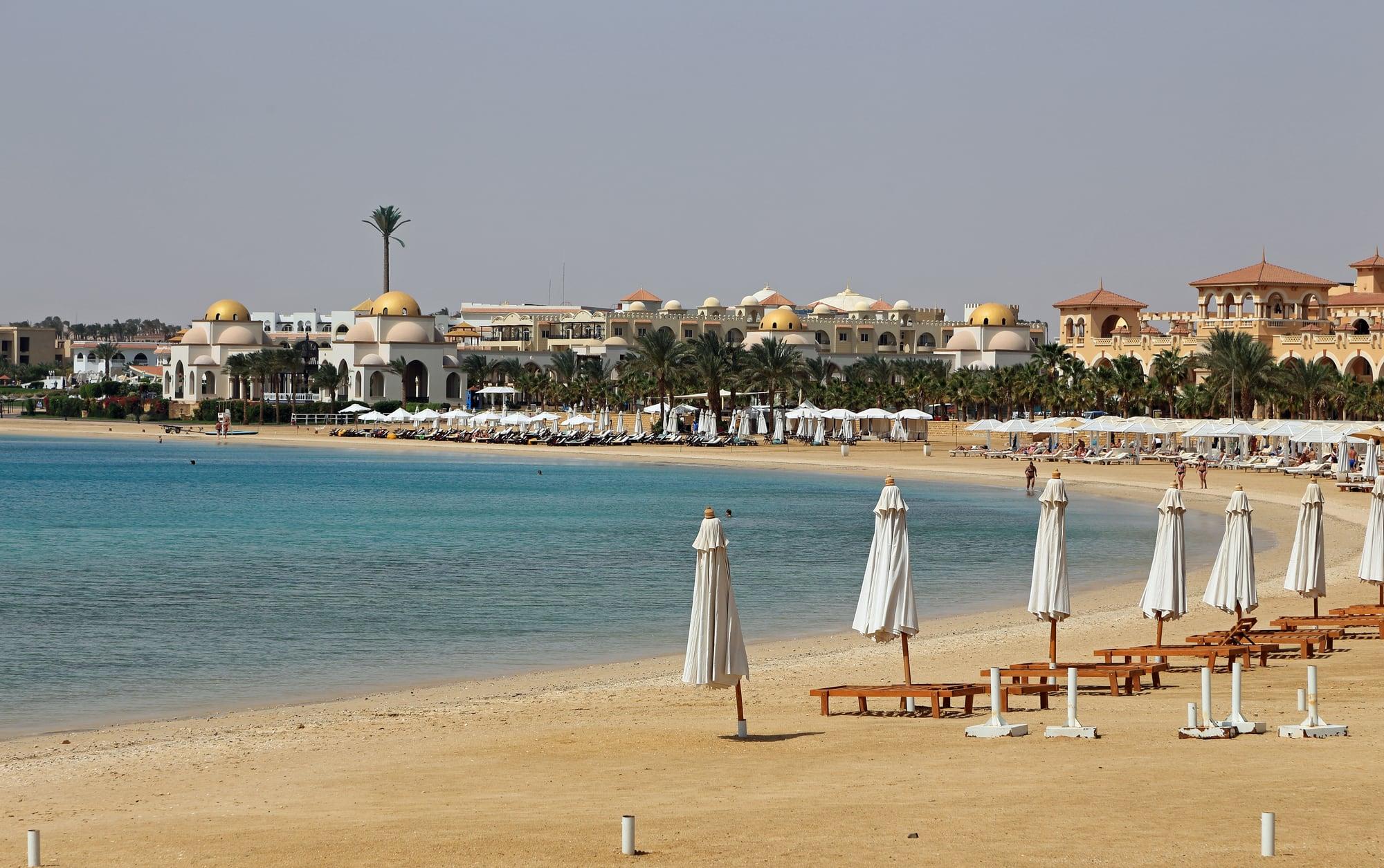 Eine ruhige türkisfarbene Bucht in Sahl Hasheesh, weiße Sonnenschirme vor kuppelgekrönten Resortgebäuden